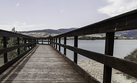 Wooden walkway leading over a lake with railings and hills in the background